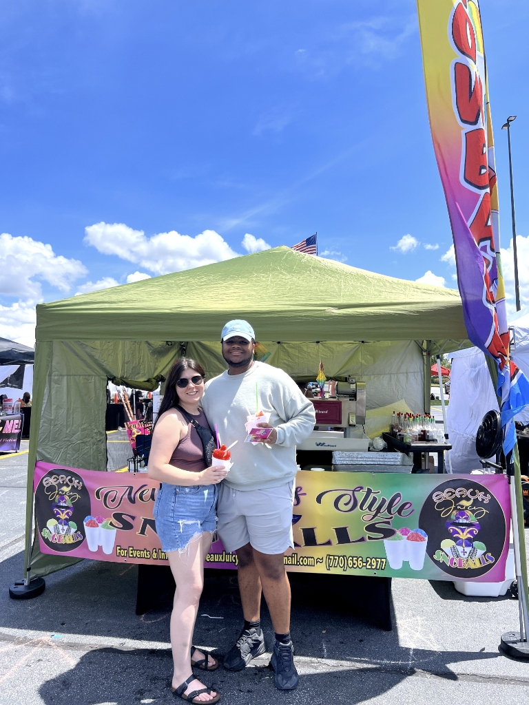 Smiling couple posing in front of Seaux Juicy banner at outdoor stand